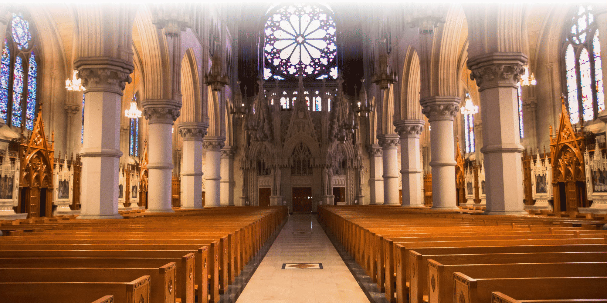 Gothic cathedral interior with rows of wooden pews, soaring stone columns, arched ceilings, and a large rose window with stained glass.