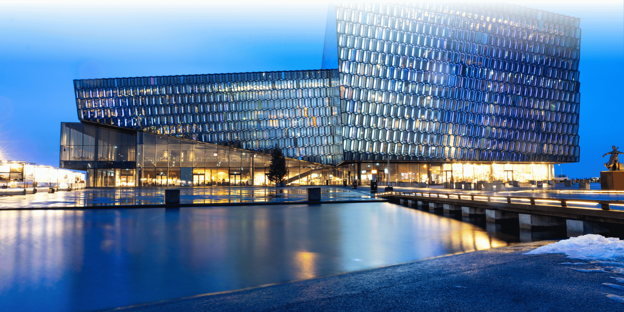 Harpa Concert Hall in Reykjavik at dusk, with its distinctive geometric glass façade illuminated and reflected in the waterfront below.