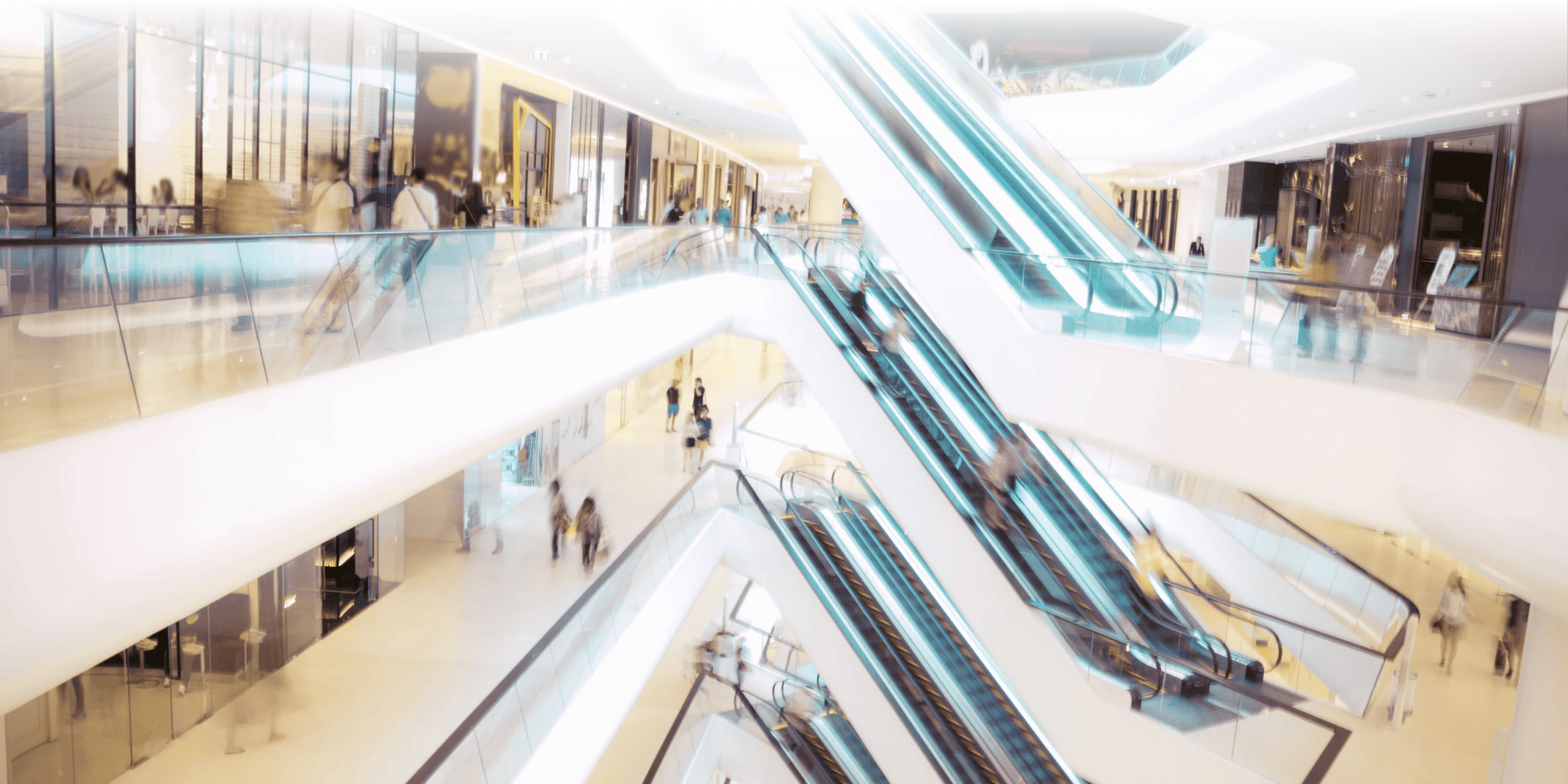 Modern shopping mall interior with criss-crossing escalators, glass balustrades and shoppers across multiple floors.