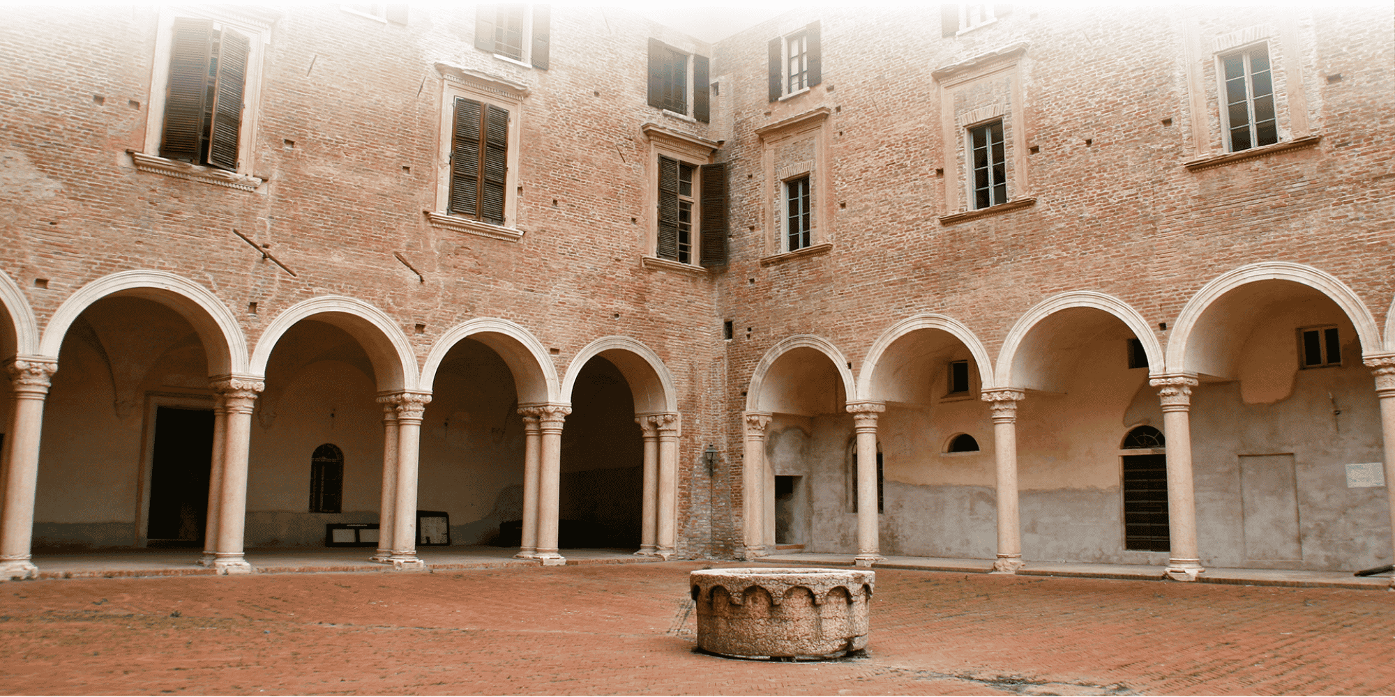 Brick courtyard with arched stone porticoes, shuttered windows, and a central stone well.