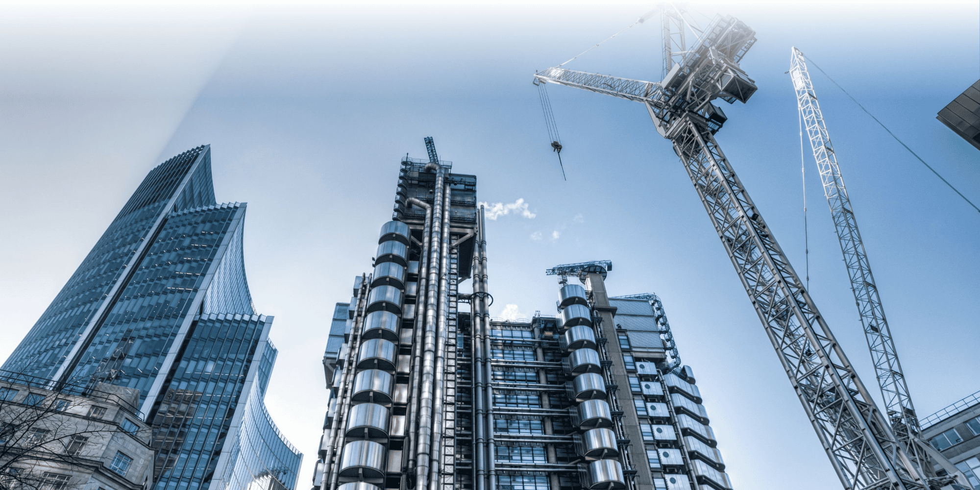 Low-angle view of modern glass and steel city skyscrapers with construction cranes