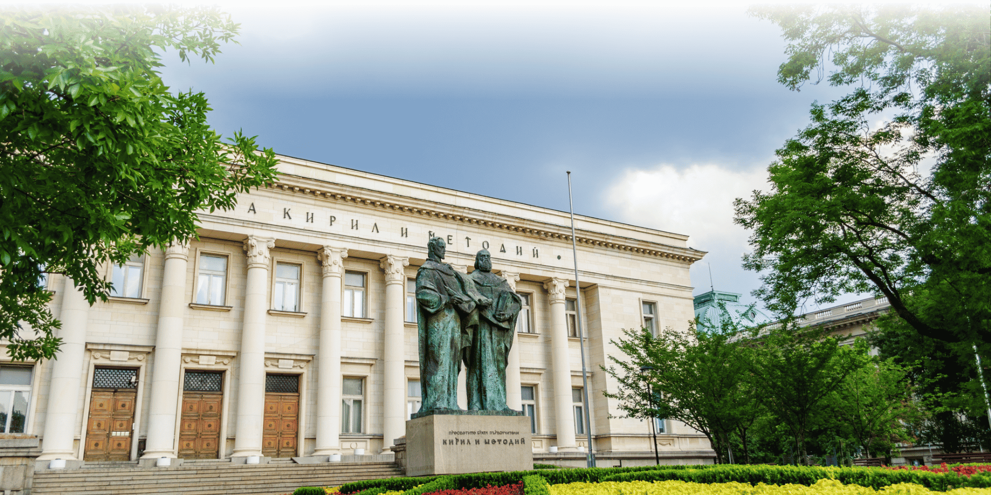 Neoclassical facade of the SS. Cyril and Methodius National Library in Sofia, Bulgaria, with columned entrance, a bronze statue of the brothers Cyril and Methodius out front, and a landscaped garden.