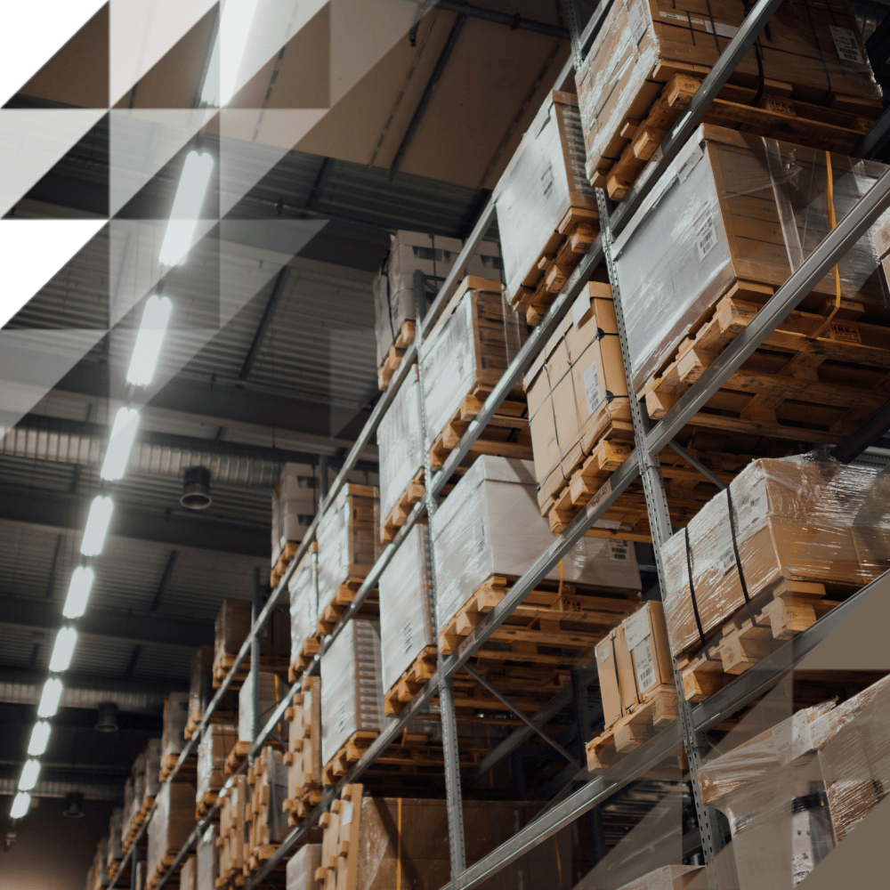 Low-angle view of multi-tiered metal shelving densely loaded with cardboard boxes and wrapped pallets, lit by ceiling strip lighting.
