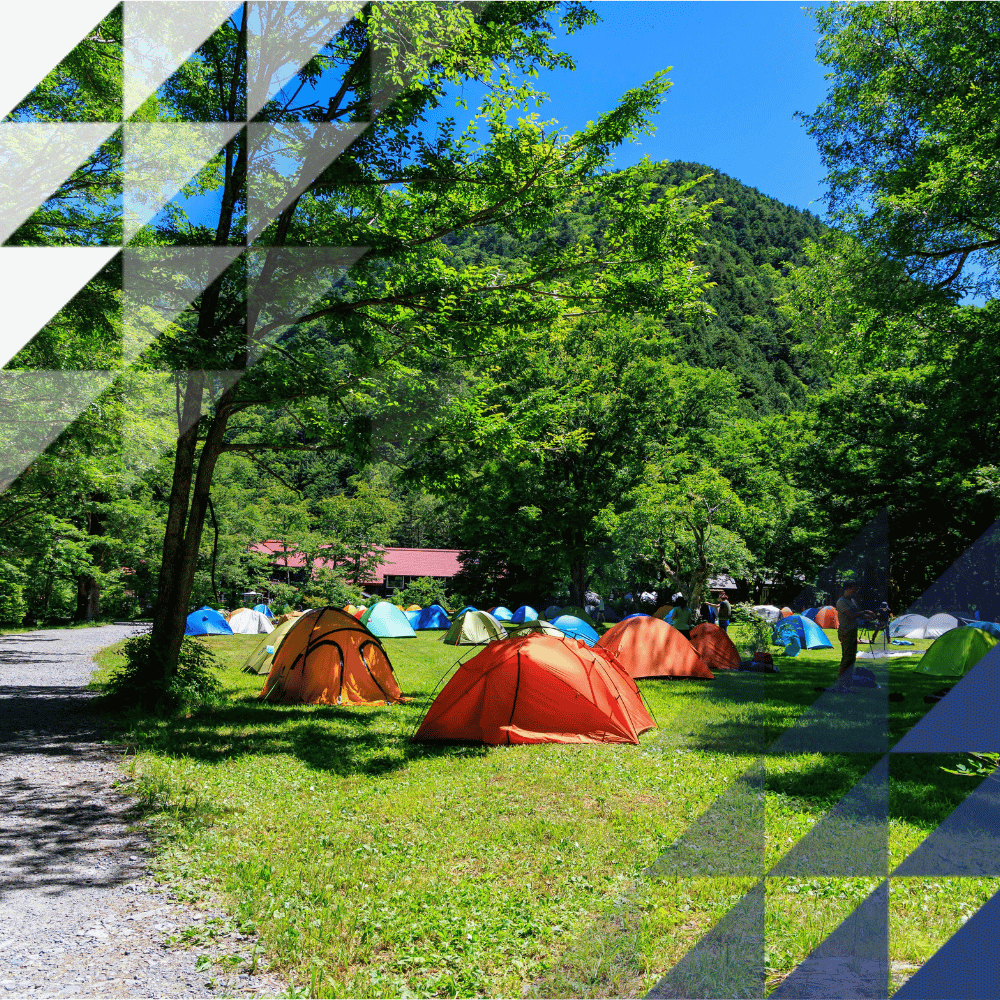Multicoloured camping tents in a forest featuring lots of trees and a gravel path. This is overlayed by Hochiki's triangle branding - dark blue and white
