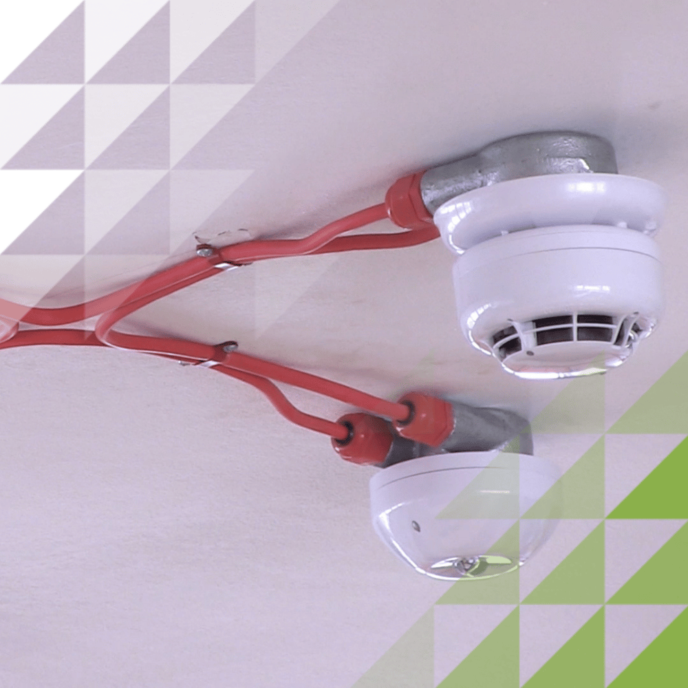 Two Hochiki smoke detectors mounted on a ceiling, connected by red fire alarm cabling that branches out from junction points above each device.