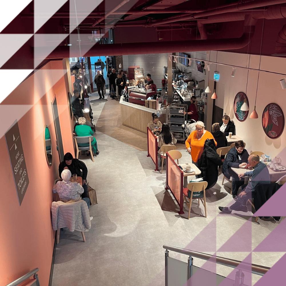 Una vista dall'alto di un caffè alla moda con pareti rosa, clienti seduti ai tavoli, un bancone di servizio e piatti decorativi appesi alle pareti.