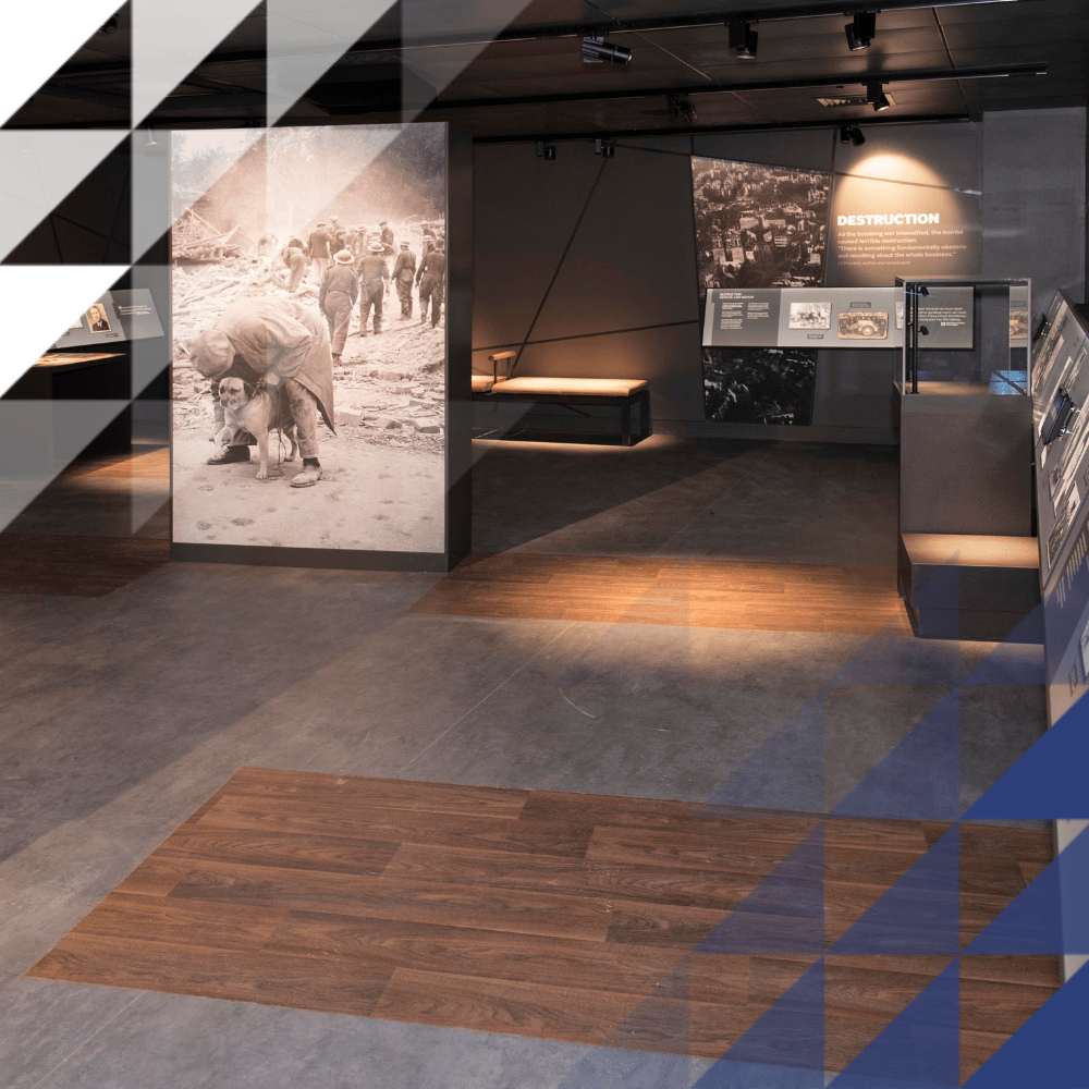 Dimly lit IBCC gallery with wartime photographs, portrait displays, illuminated panels on 