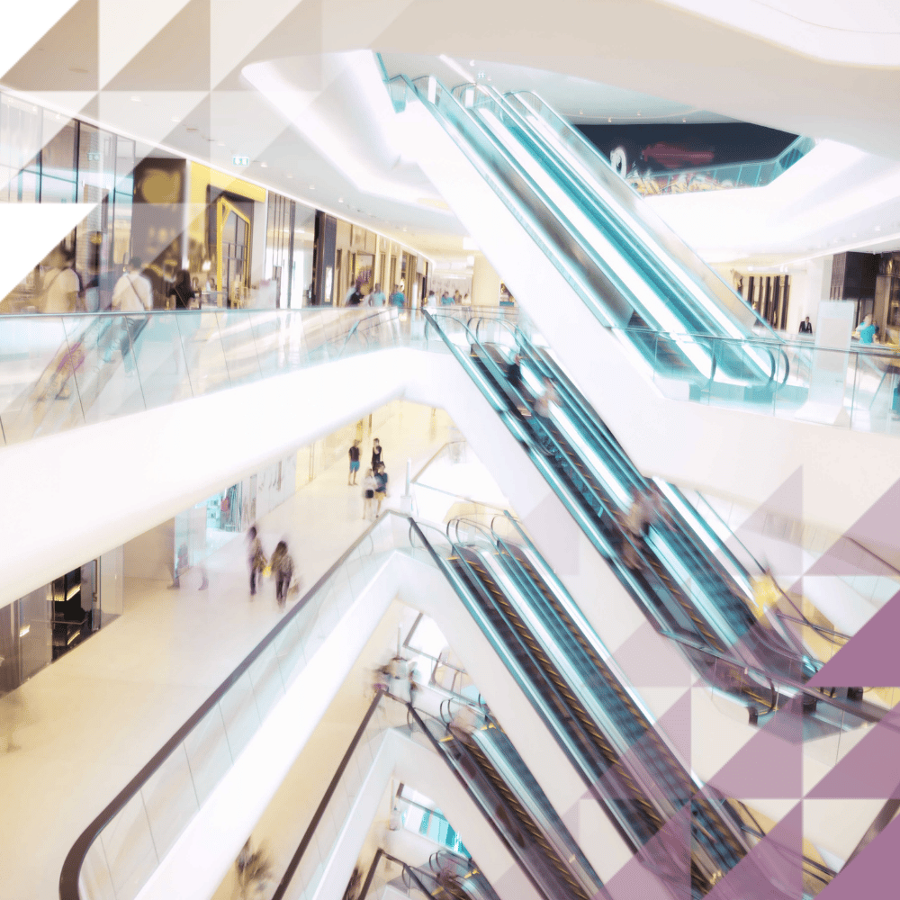 Modern shopping mall interior with criss-crossing escalators, glass balustrades and shoppers across multiple floors.