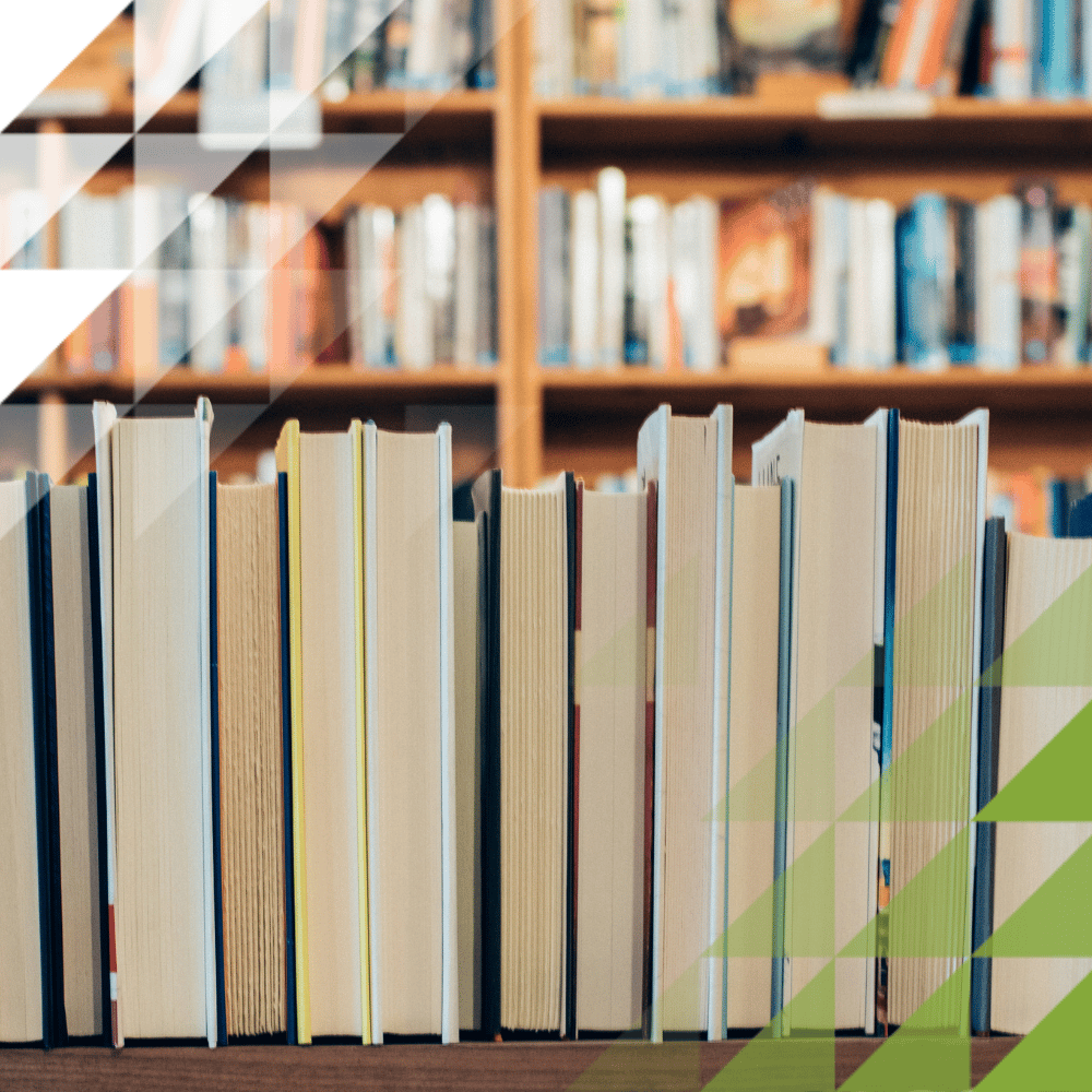 A close-up of upright book spines in the foreground with shelves of colourful books softly blurred behind.
