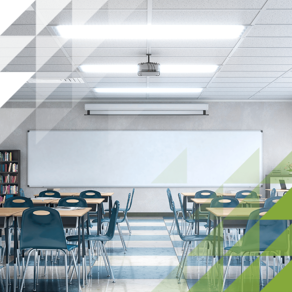 Bright classroom with rows of teal chairs at individual desks, a whiteboard, overhead projector, bookcase and wall-mounted air conditioning unit.