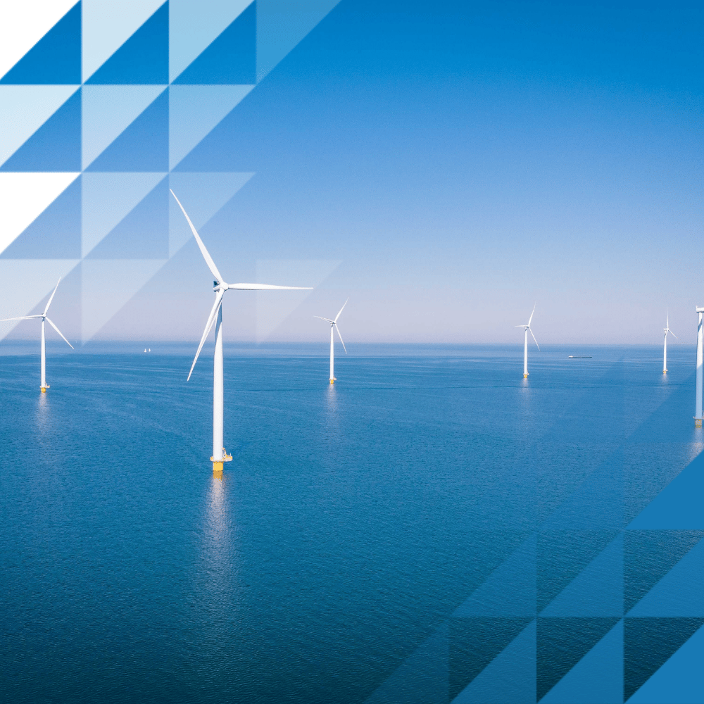 Una fila di turbine eoliche offshore bianche che si ergono su un mare calmo e di un blu intenso, sotto un cielo limpido e azzurro.