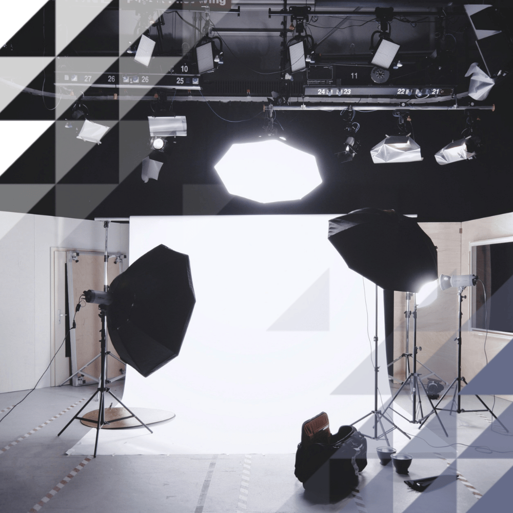 A professional photography studio with a white seamless backdrop, softbox lighting rigs on stands, an overhead ceiling-mounted lighting grid, and camera equipment on the floor.