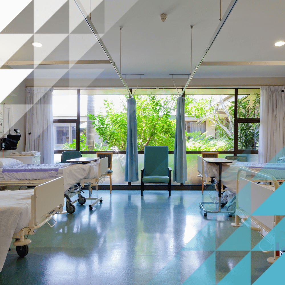 Un luminoso reparto ospedaliero con letti d'ospedale, una poltrona color verde acqua e tende per garantire la privacy, da cui si affaccia su un giardino rigoglioso attraverso ampie finestre.