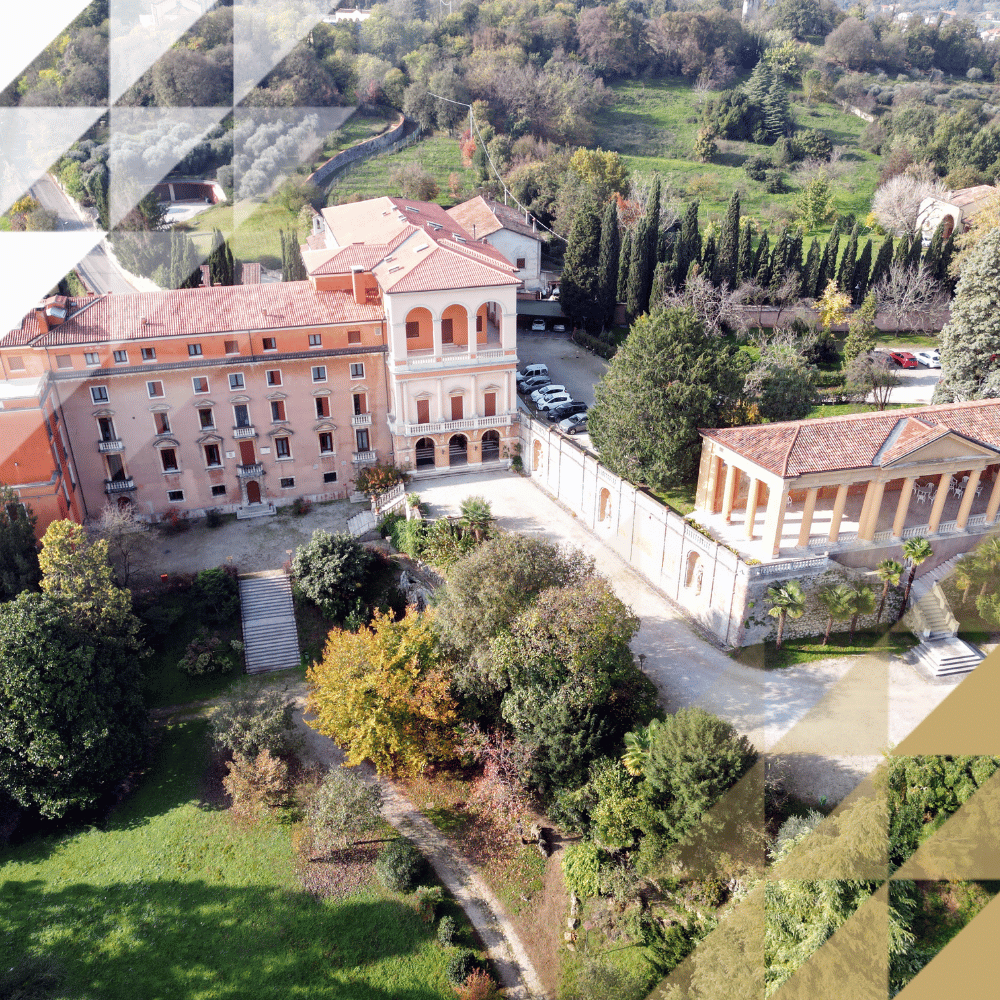 Vista aerea di una maestosa villa italiana con tetti in terracotta, circondata da alberi secolari, giardini e un parco fiancheggiato da cipressi in autunno