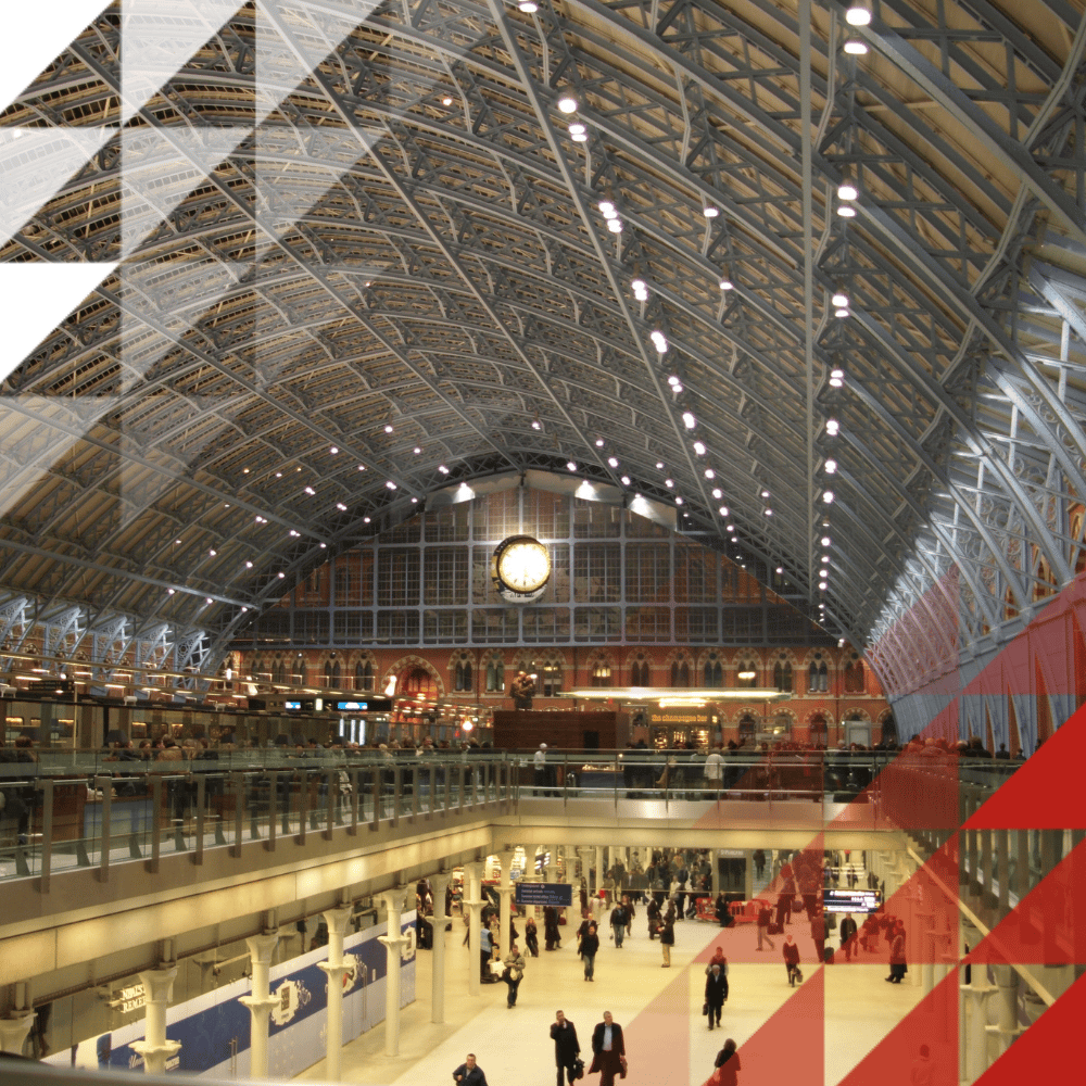 Interior of St Pancras railway station, showing its vaulted glass-and-iron roof, a large clock, upper-level shops and bars, and travelers on the concourse below.