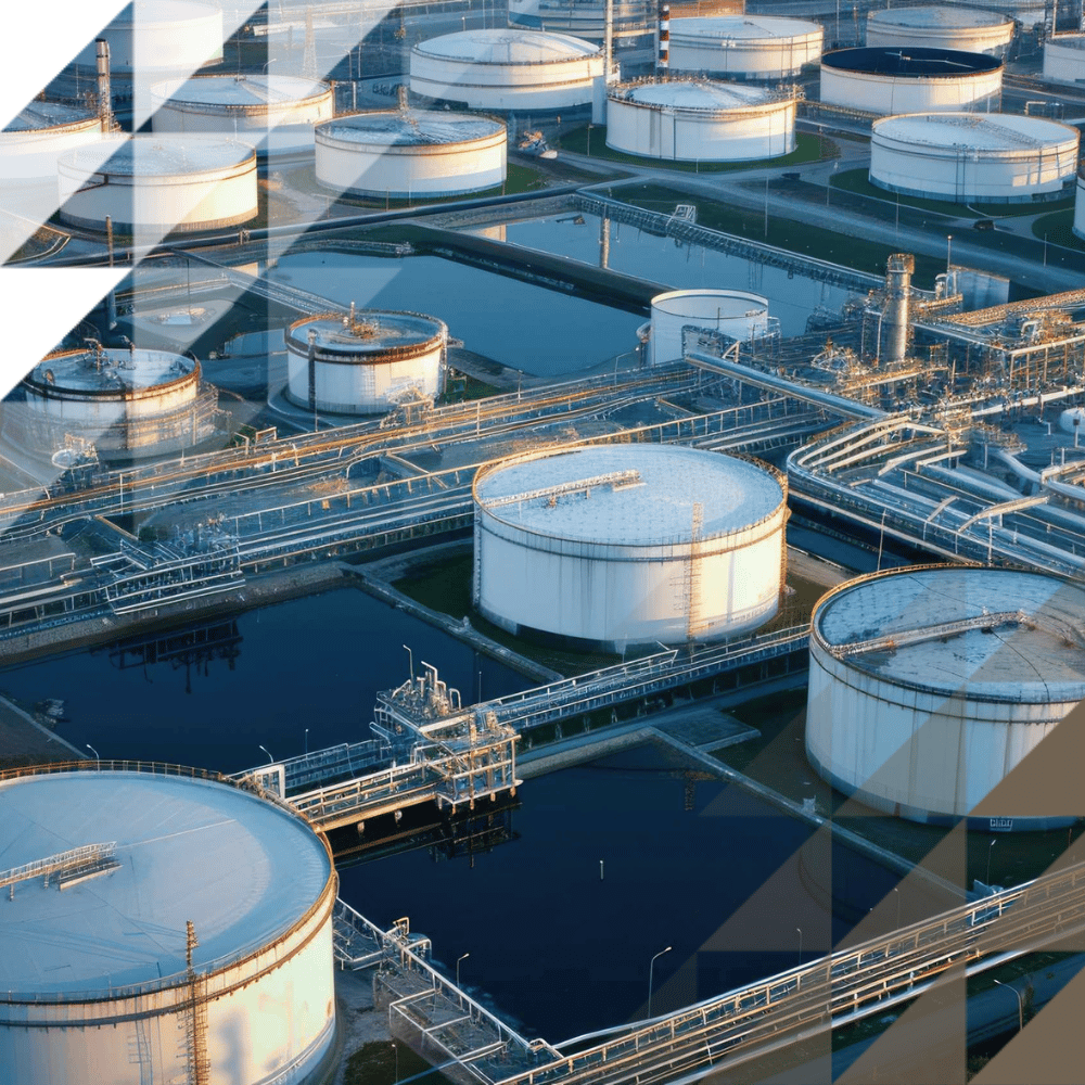Aerial view of petrochemical site with cylindrical white storage tanks, pipelines, walkways and containment pools in warm evening light.