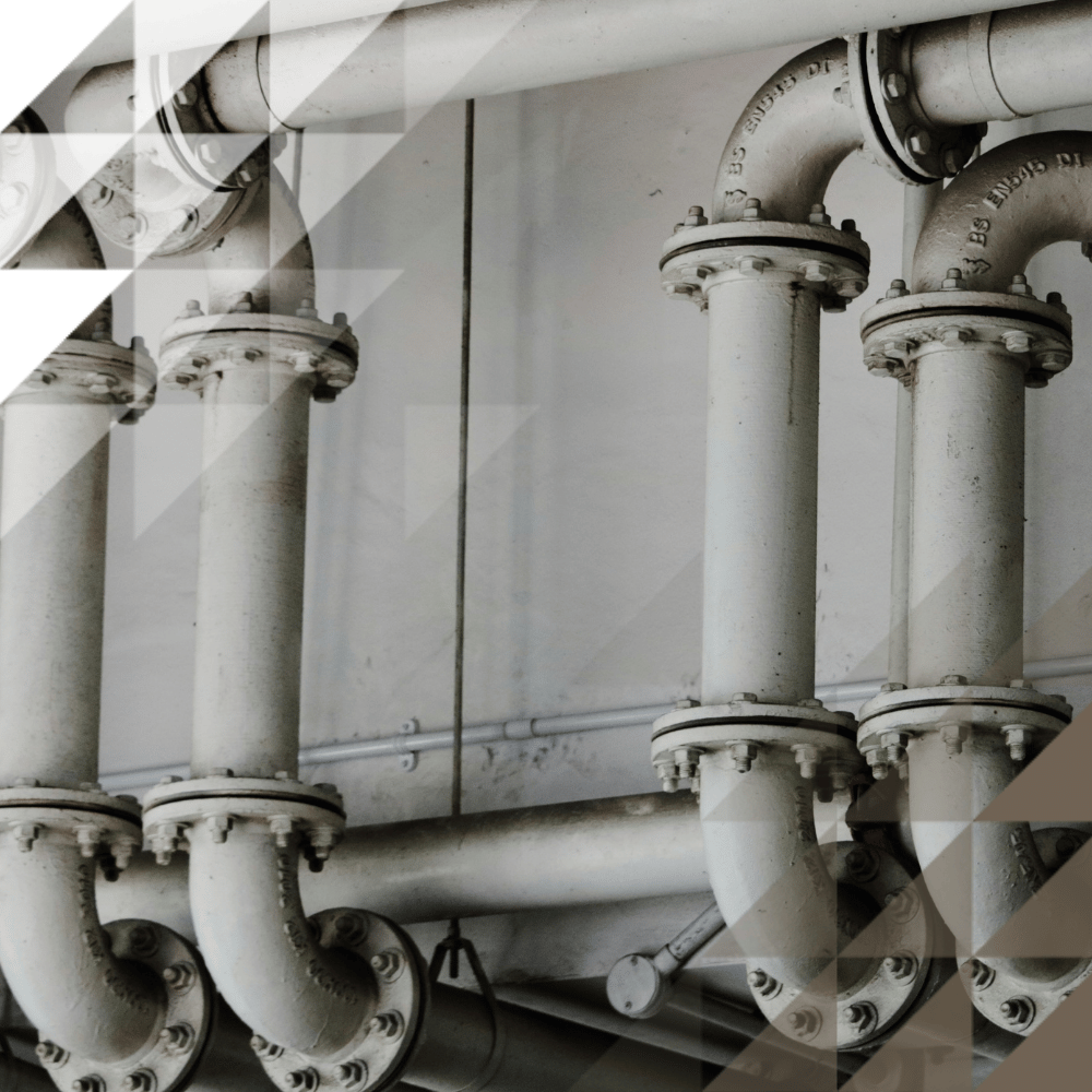 Black-and-white close-up of industrial pipework, showing several vertical pipes connected with bolted flange joints against a wall.