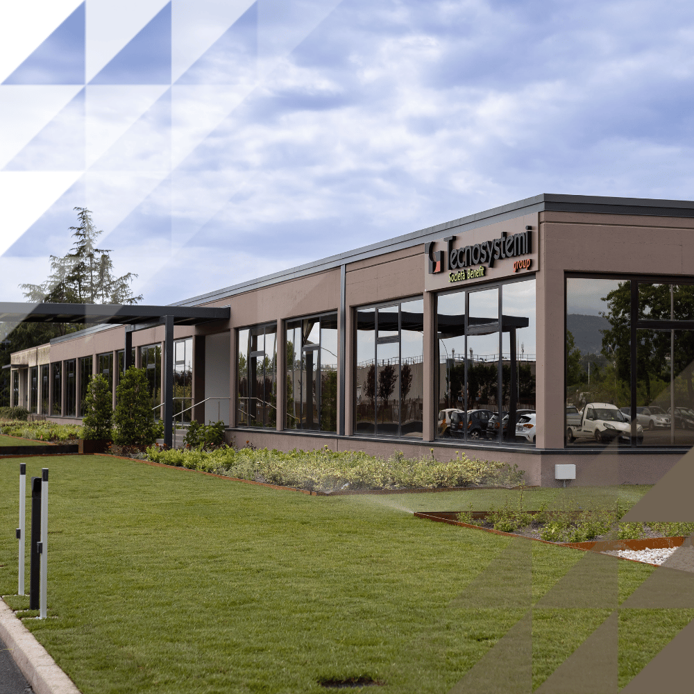 Exterior of the Tecnosystemi Group headquarters, a modern single-storey commercial building with large glass façade, manicured lawn, and planted borders.