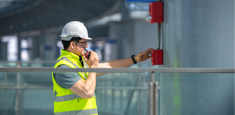 Man in hard hat and holding walkie talkie checking out fire alarm