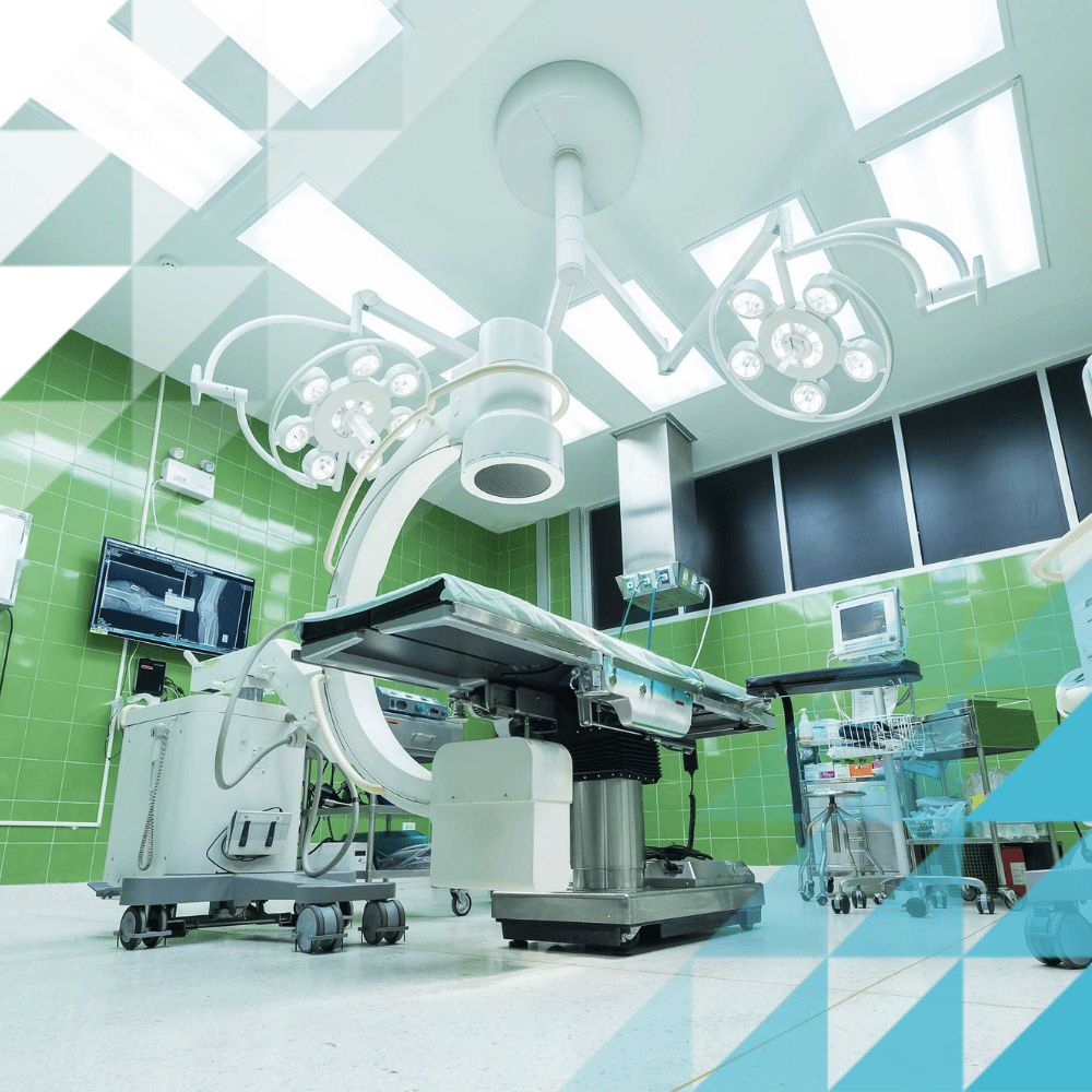 Modern surgical suite with C-arm imaging equipment, operating table, and overhead surgical lights in a green-tiled theatre.